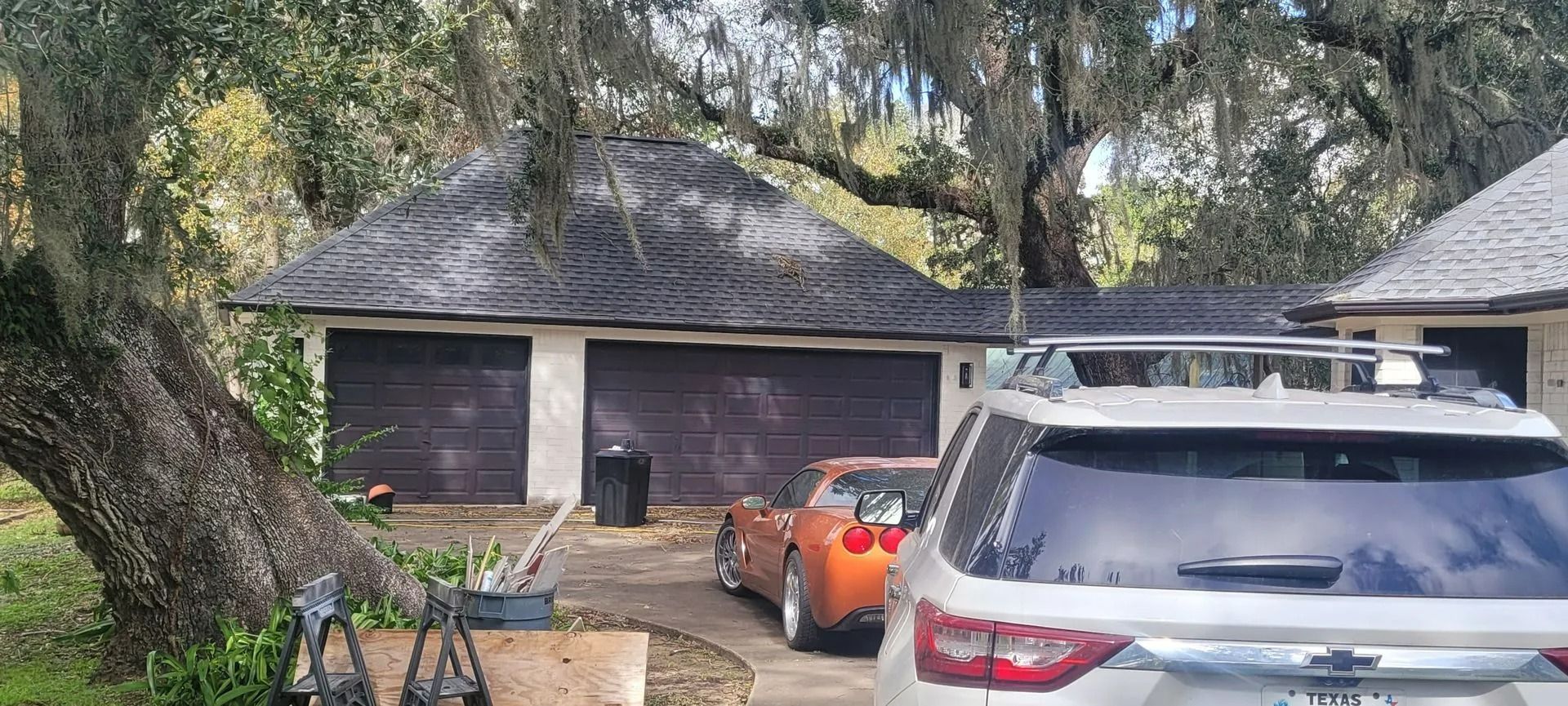 A two-car garage with dark brown doors, an orange sports car, and a silver SUV parked in the driveway.