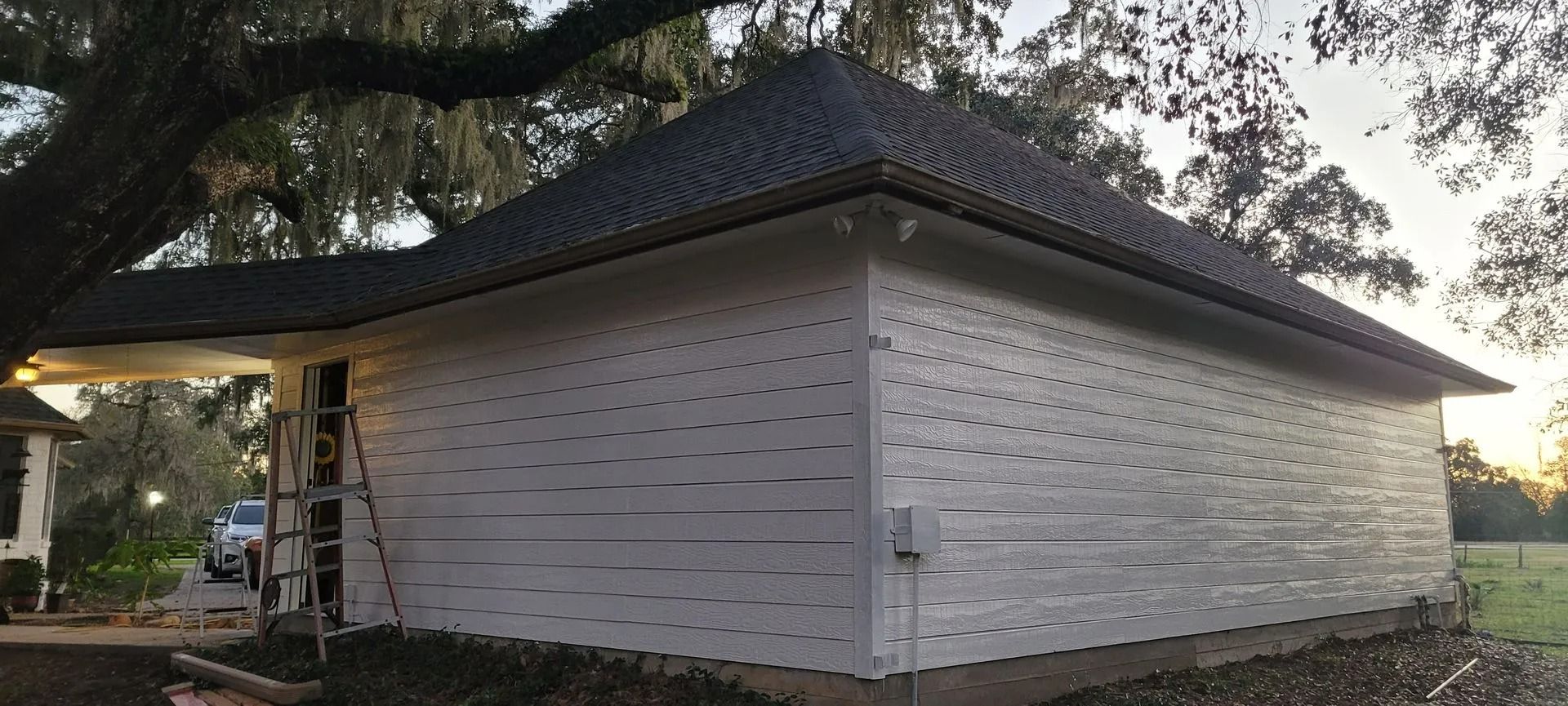 White building with dark roof and evenly spaced holes in the siding.  Trees in background.