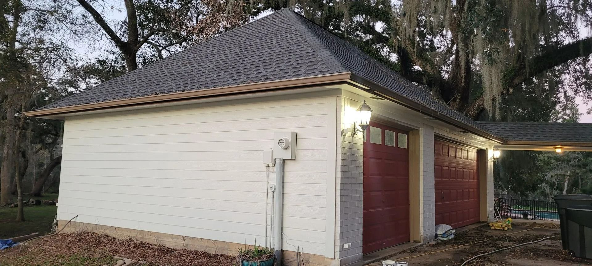 White garage with red doors, black roof, and trees in background.