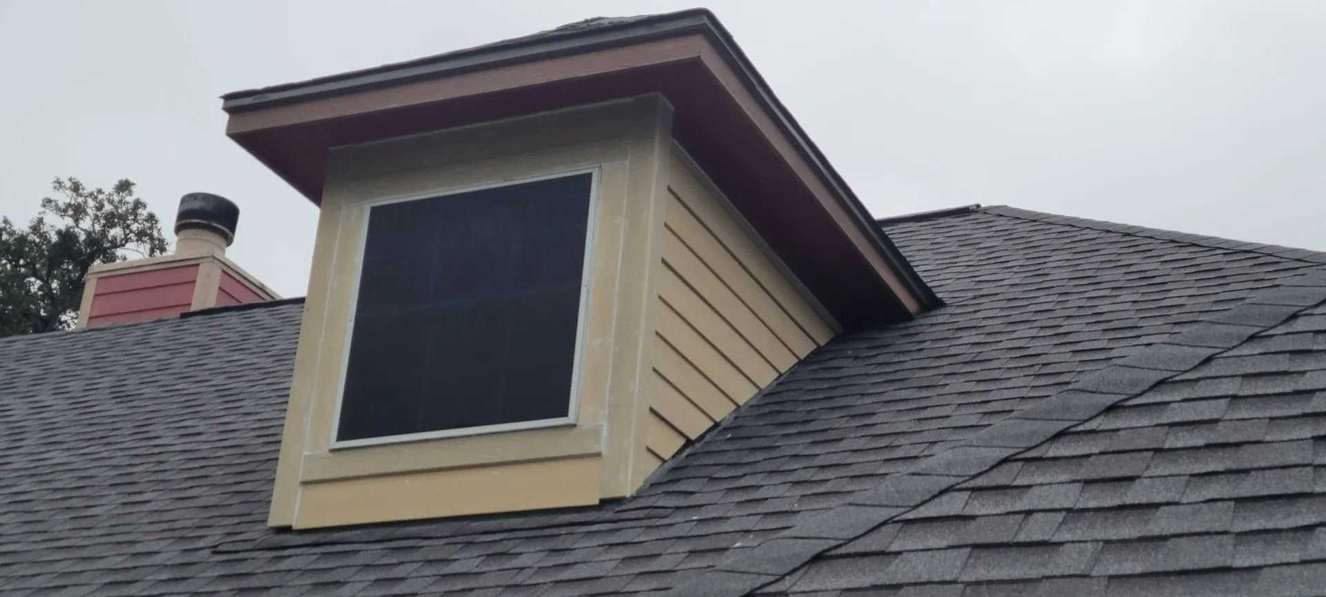A dormer window on a shingled roof under an overcast sky.