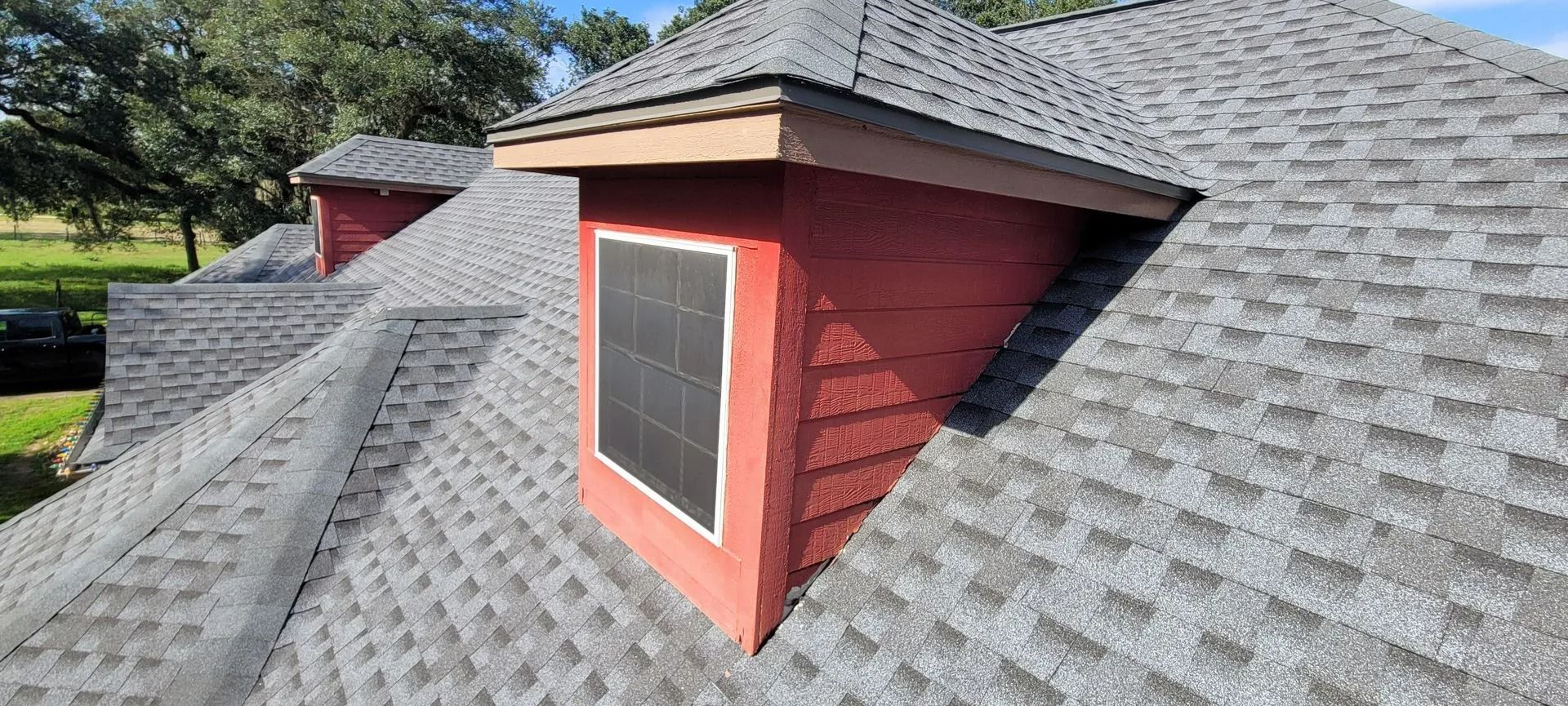 Red dormer with window on gray shingled roof under blue sky.