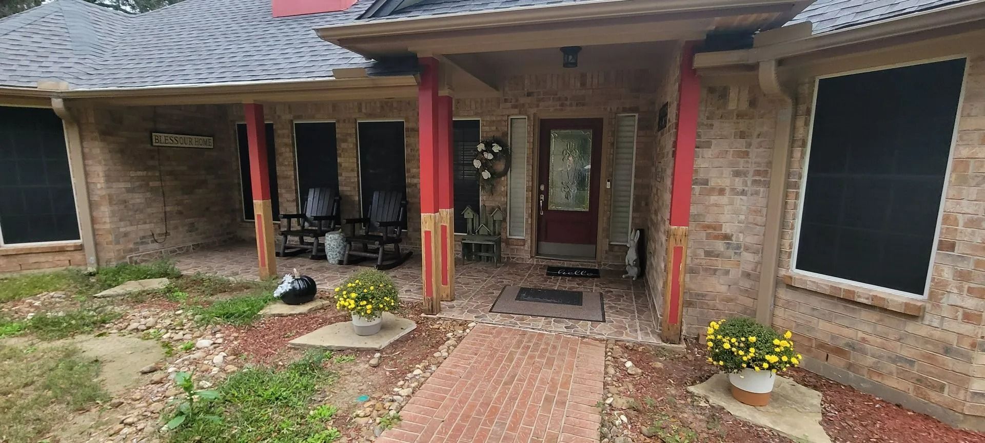 Exterior of a brick home with red columns and a brick path leading to the front door.