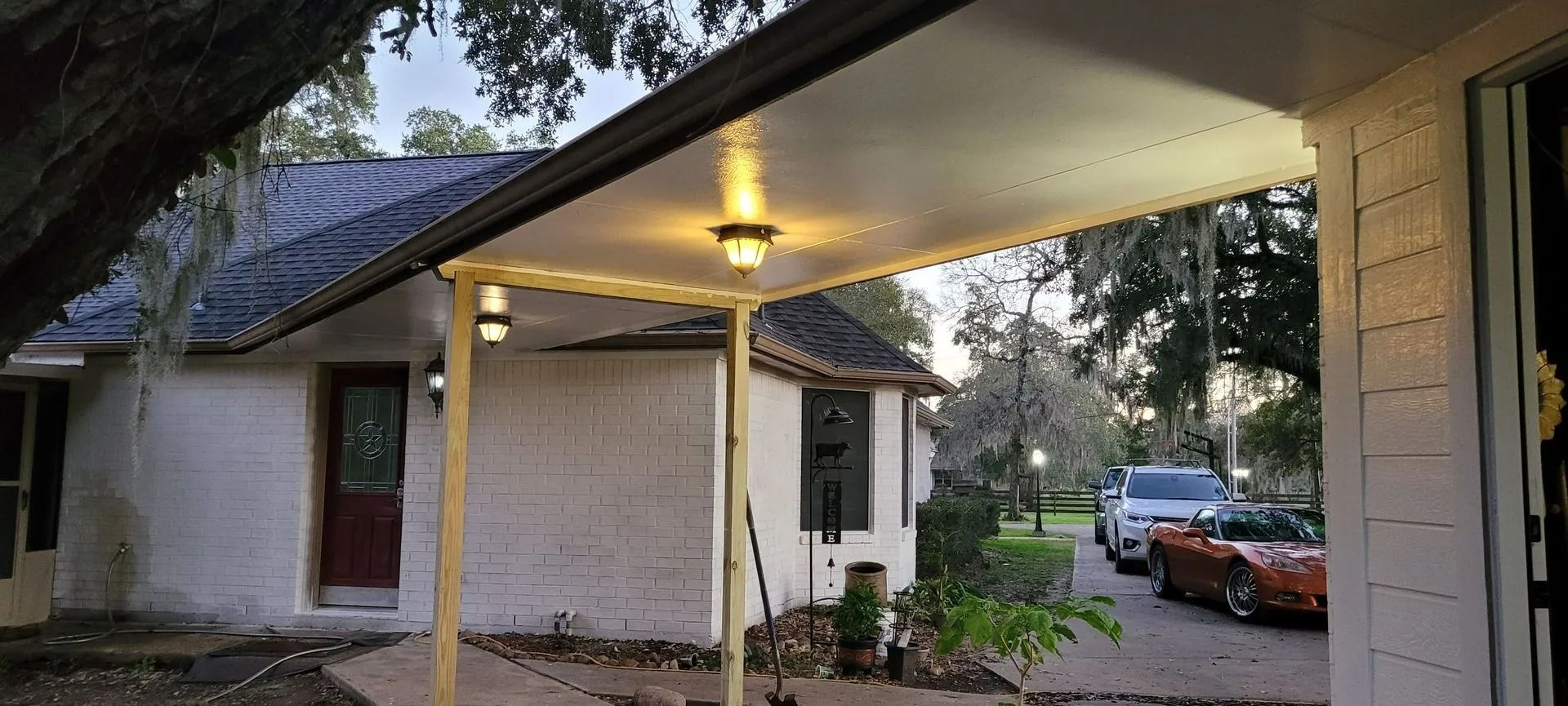 Exterior view of a white brick house with a porch and two cars parked in the driveway.