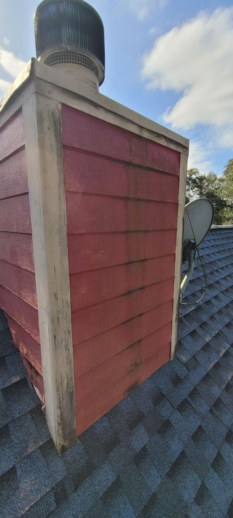 Red chimney with wooden siding, light trim, and a roof-mounted satellite dish.
