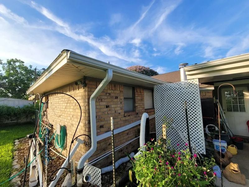 Exterior view of a brick house with white gutters. Blue sky with clouds overhead.