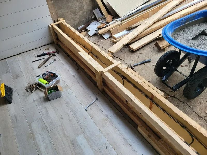 Wooden formwork with rebar, prepared for concrete pouring. Wheelbarrow with concrete mix, tools and construction debris.