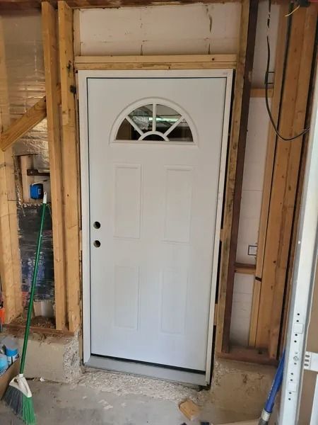 White door installed in a rough wooden frame, unfinished basement setting.