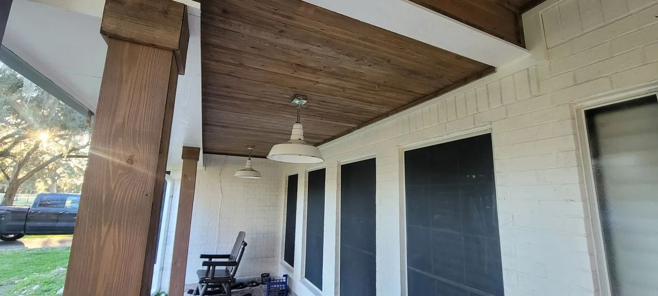 Covered porch with wood ceiling and brick walls, two hanging lights, and a rocking chair.