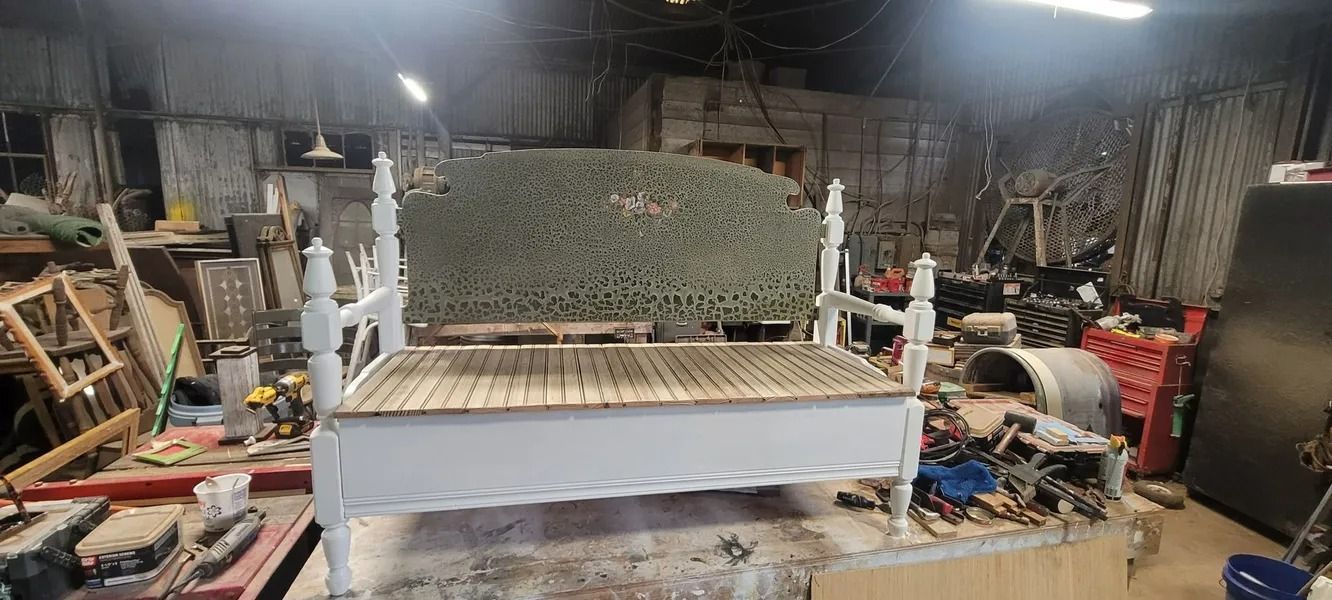 A white bench with spindles in a cluttered workshop. Wood and tools are scattered around.