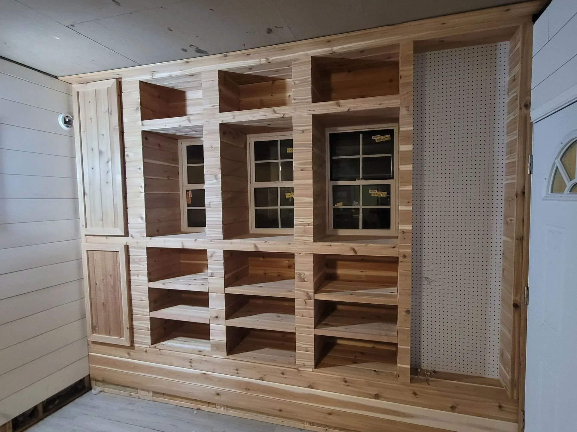 Built-in wooden shelving unit with windows and pegboard, in a room with white walls and a door.