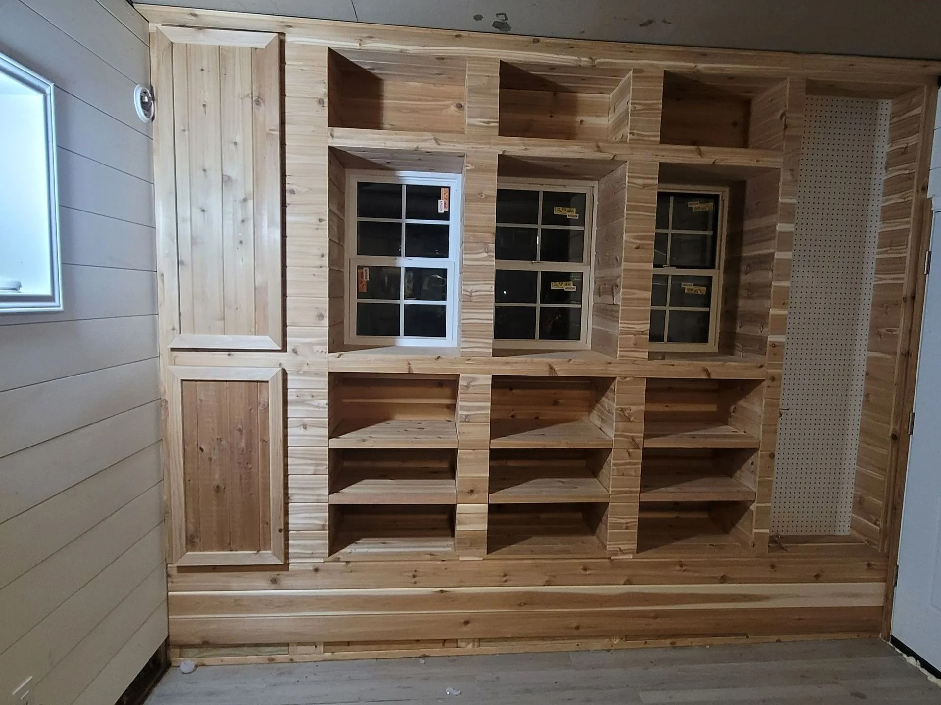 Wooden built-in shelving and cabinets with two windows; construction in progress.