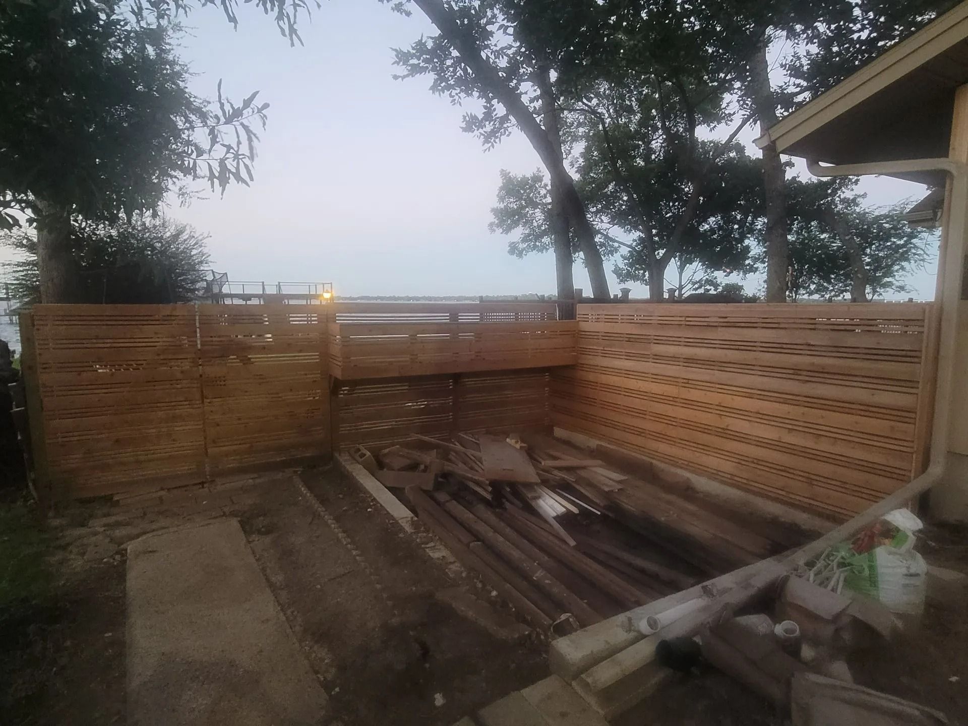 Wooden fence surrounding a deck with water and trees visible in the background.