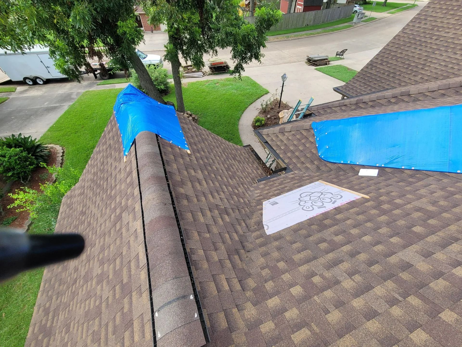 Brown shingled roof with blue tarps, a paper, and a camera; outdoors on a sunny day.