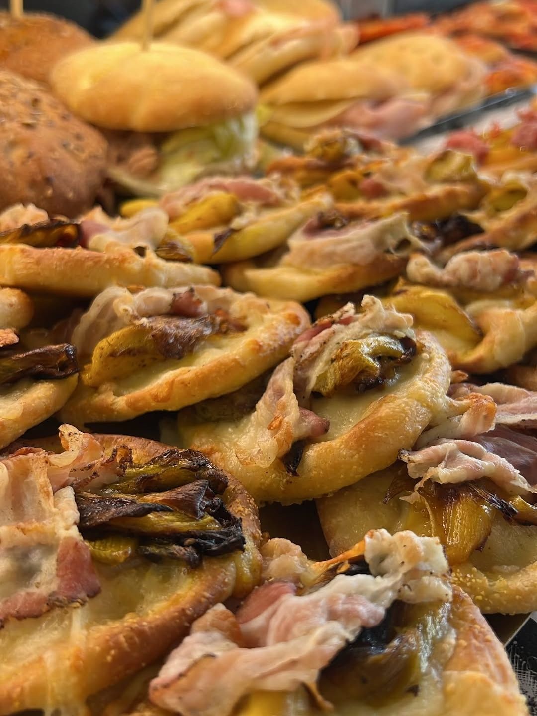 Primo piano di prodotti da forno, tra cui piccole pizze con condimenti come pancetta e funghi.