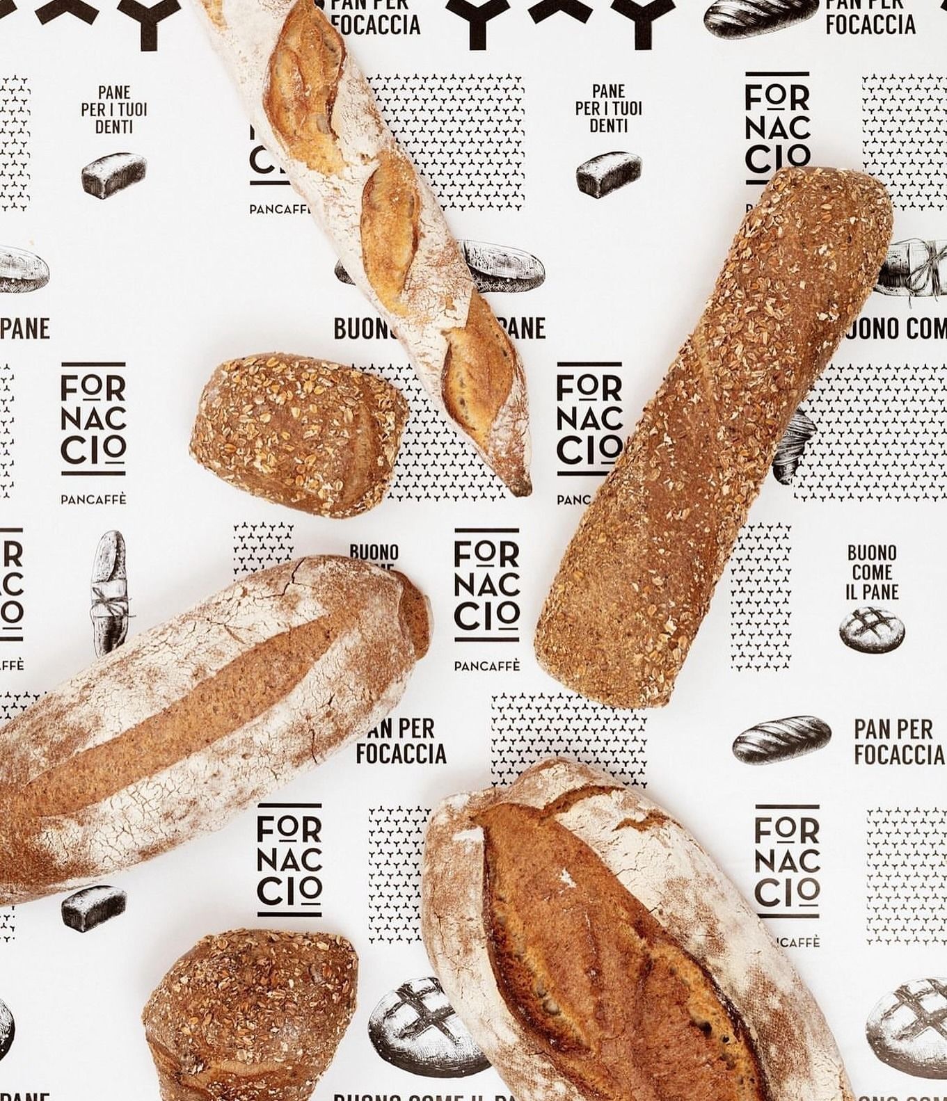 Varie pagnotte di pane e panini su una superficie bianca stampata, alcune delle quali recano l'etichetta 