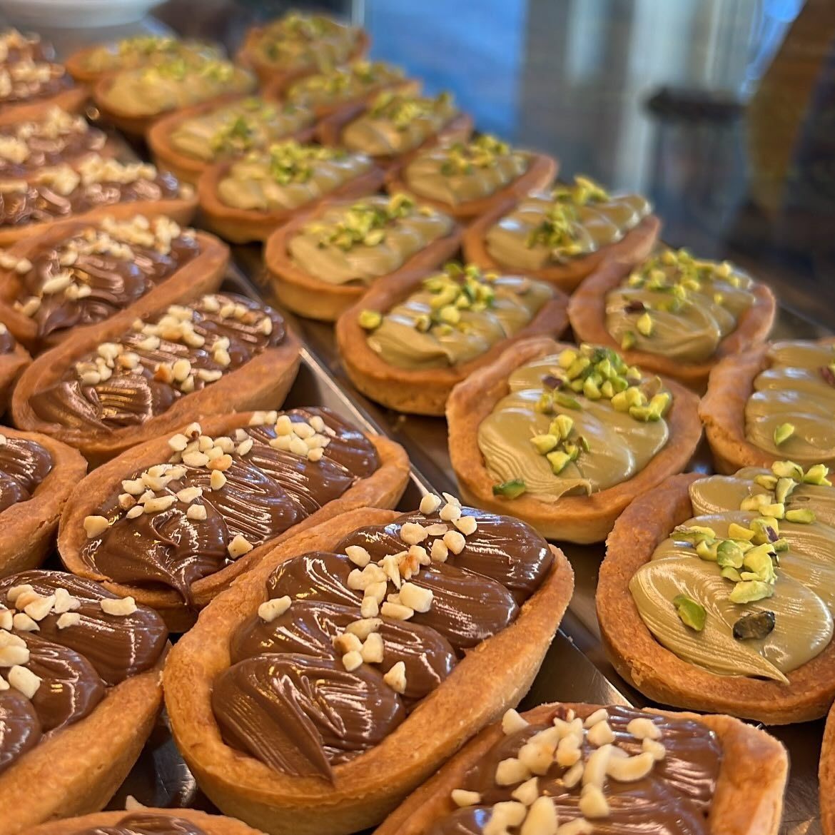 File di pasticcini ovali ripieni di crema al cioccolato e pistacchio, ricoperti di noci.