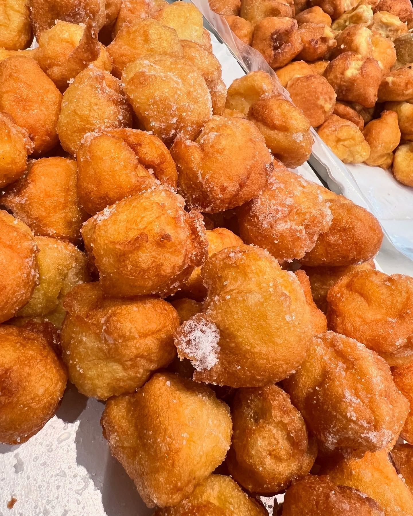 Palline di pasta fritte, dorate e ricoperte di zucchero, disposte su una superficie bianca.