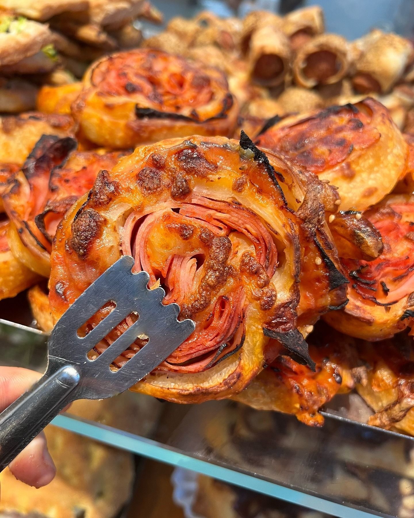 Rotolo di pasta sfoglia salata con prosciutto, formaggio e pomodoro a vista, prelevato con un utensile da portata.