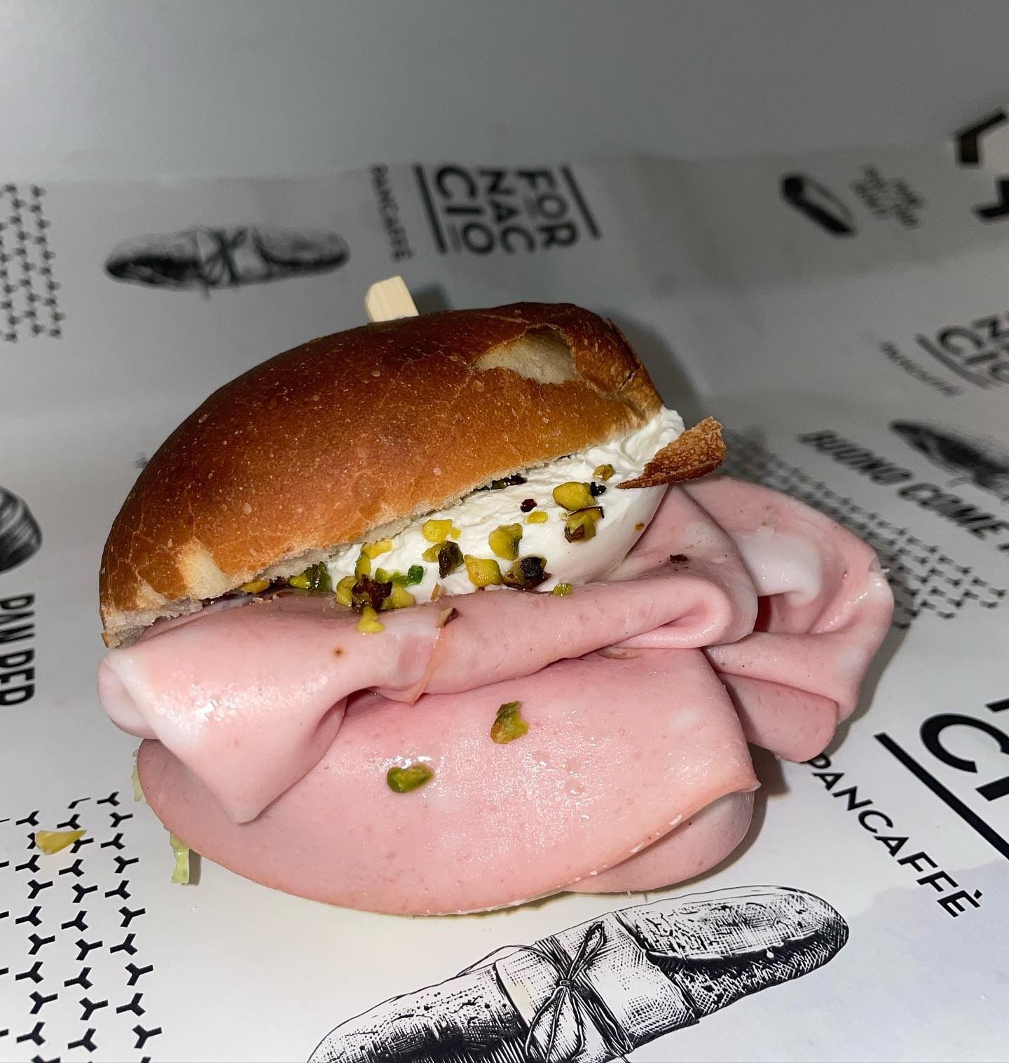 Panino con mortadella, panna e pistacchio su carta bianca.