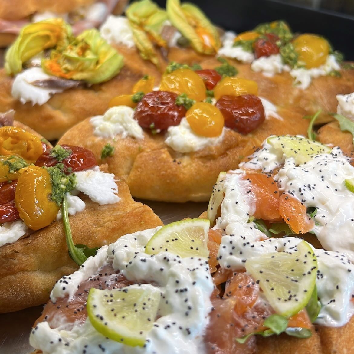 Primo piano di vari tipi di focacce italiane farcite con pomodori, formaggio, fiori e salmone.