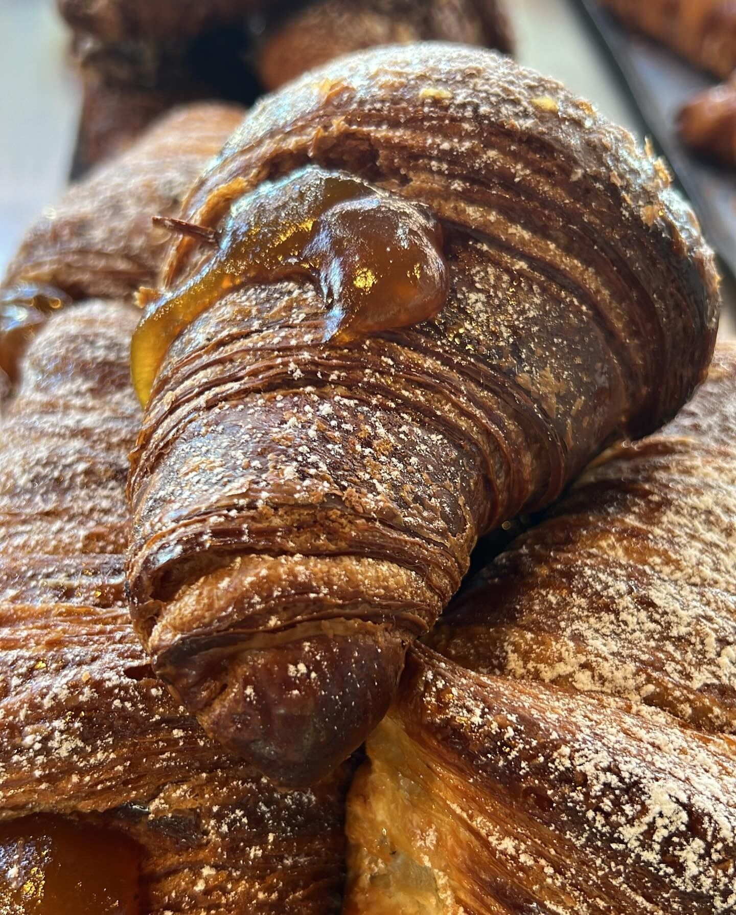 Primo piano di un croissant sfogliato spolverato con zucchero a velo e ricoperto di caramello.