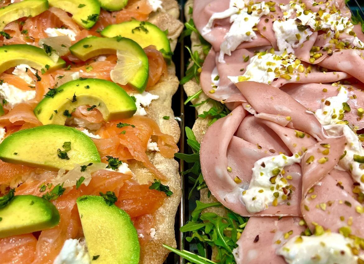 Due focacce: una con avocado e salmone, l'altra con mortadella, entrambe condite con formaggio.