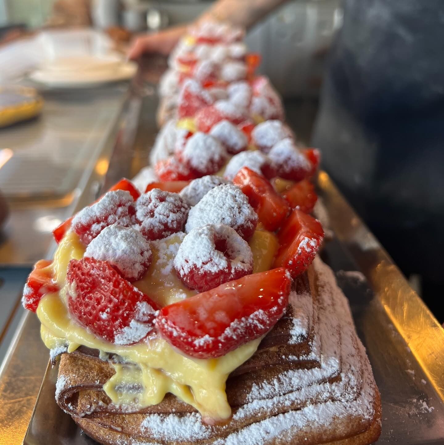 Pasta sfoglia guarnita con fragole, lamponi e zucchero a velo su un vassoio di metallo.
