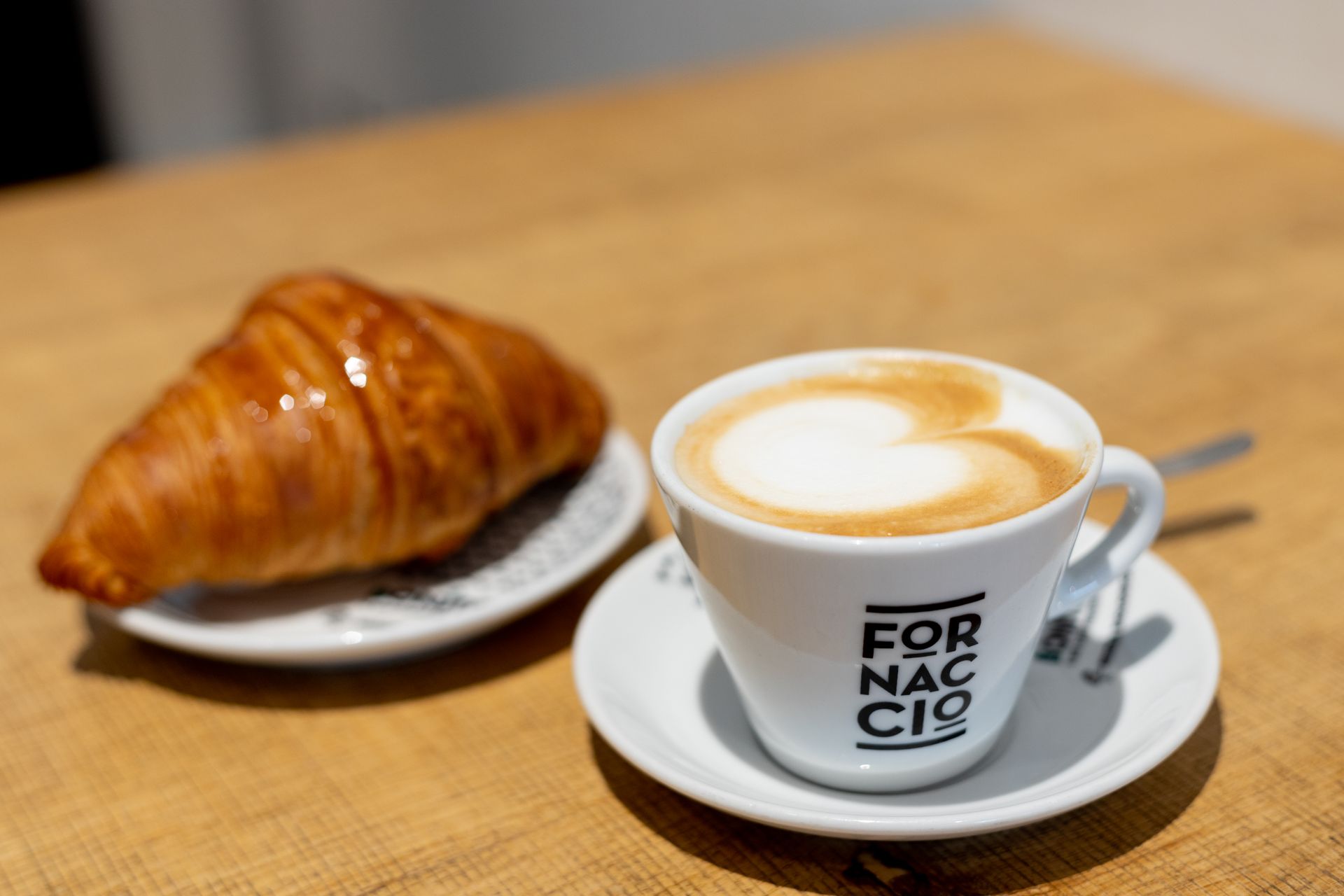 Tazza di cappuccino con disegno a cuore e croissant su un tavolo di legno.