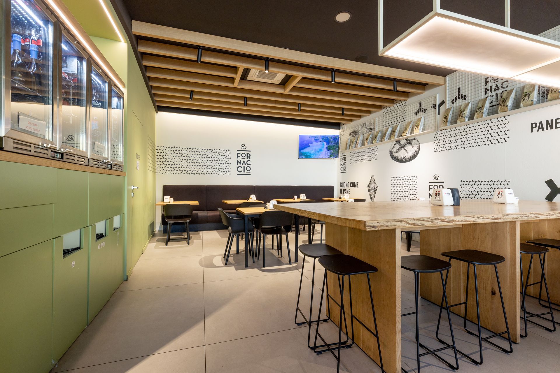 Interno del ristorante con tavoli in legno, sgabelli neri e pareti decorate.