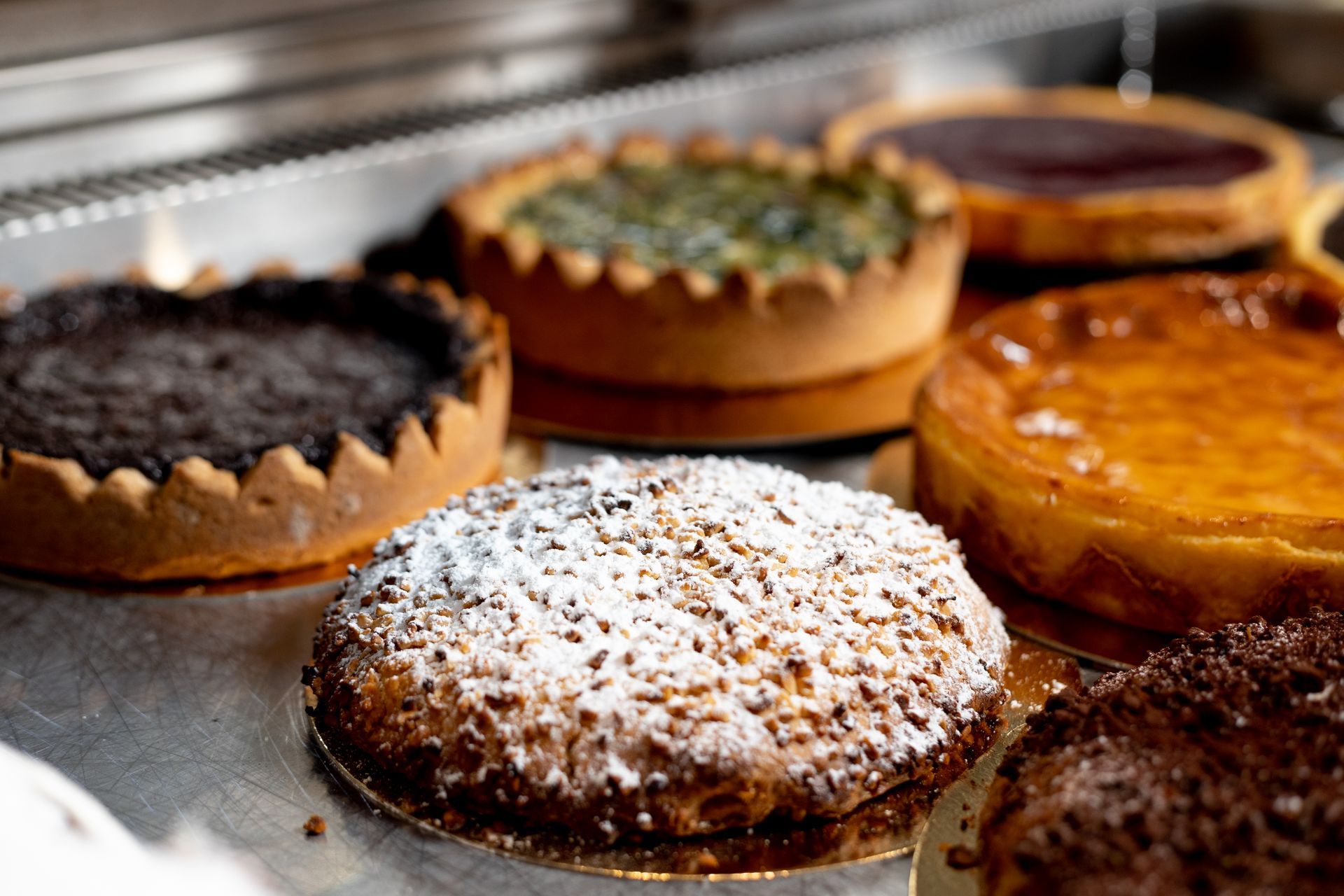 Mano che solleva un rotolo di prosciutto e formaggio al forno, mostrandone gli strati. Esposizione di prodotti da forno, altri dolci sullo sfondo.
