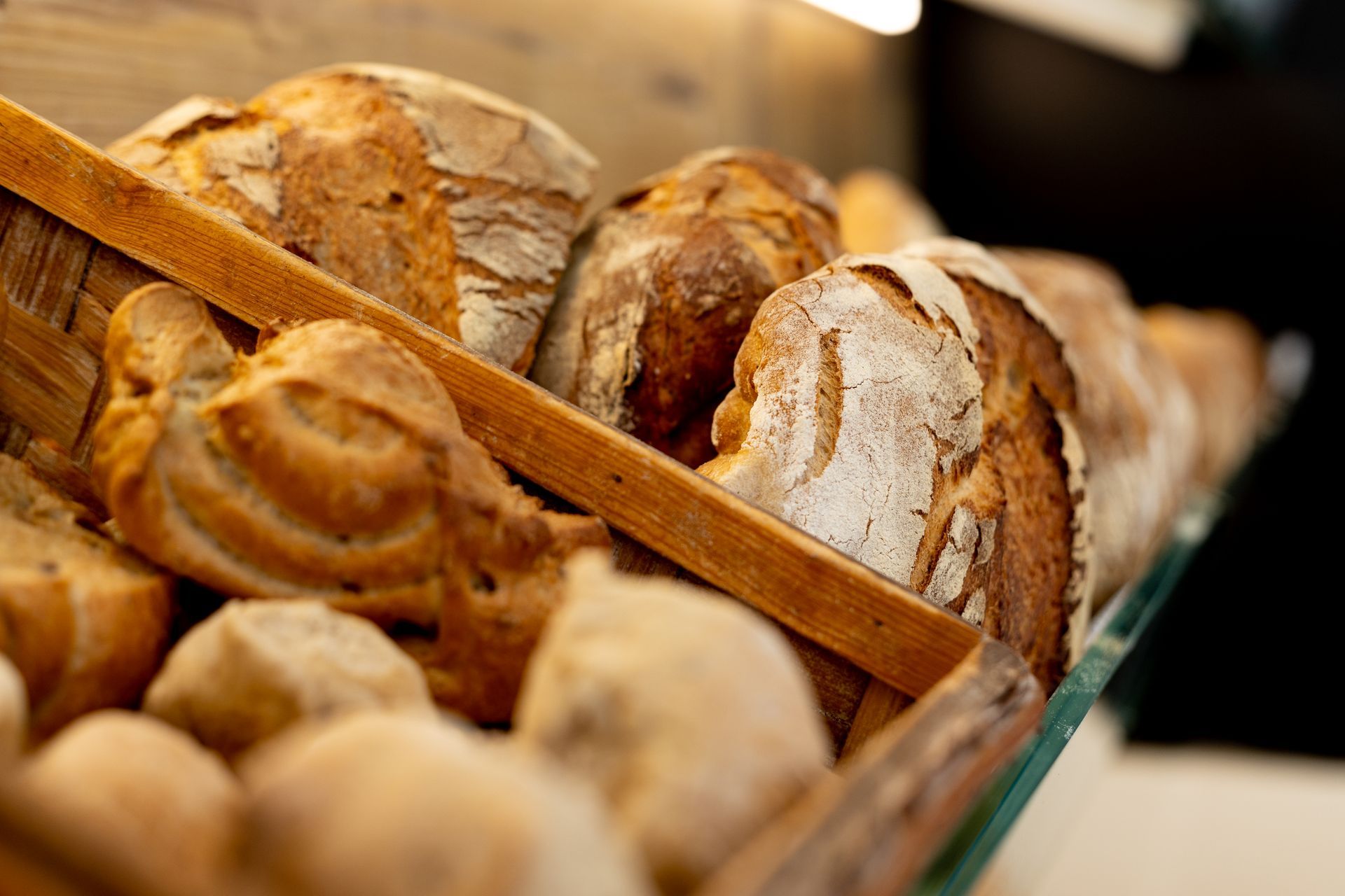 Varie pagnotte di pane croccante esposte in un espositore di legno.