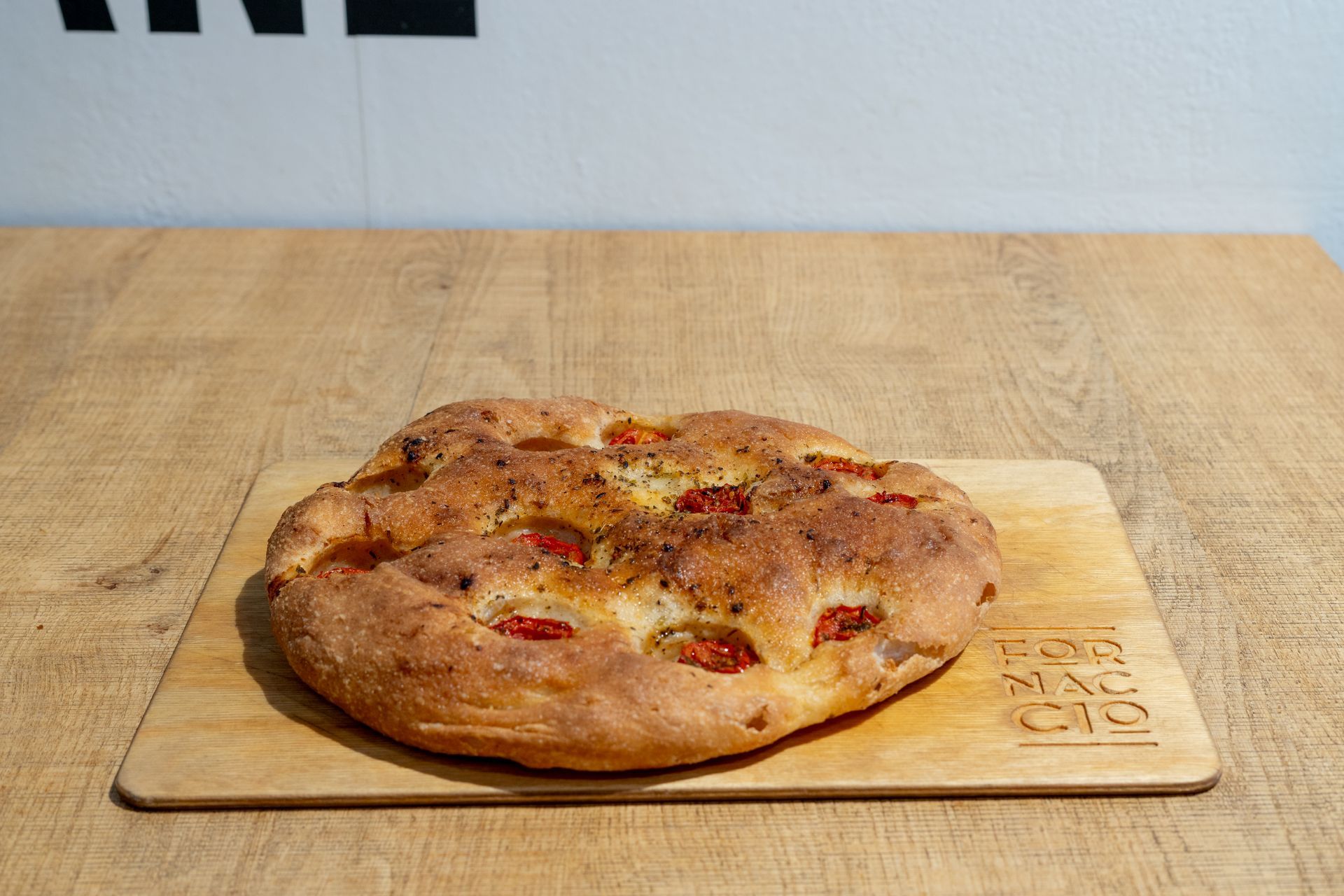 Focaccia con pomodori ed erbe aromatiche su un tagliere di legno su un tavolo di legno.