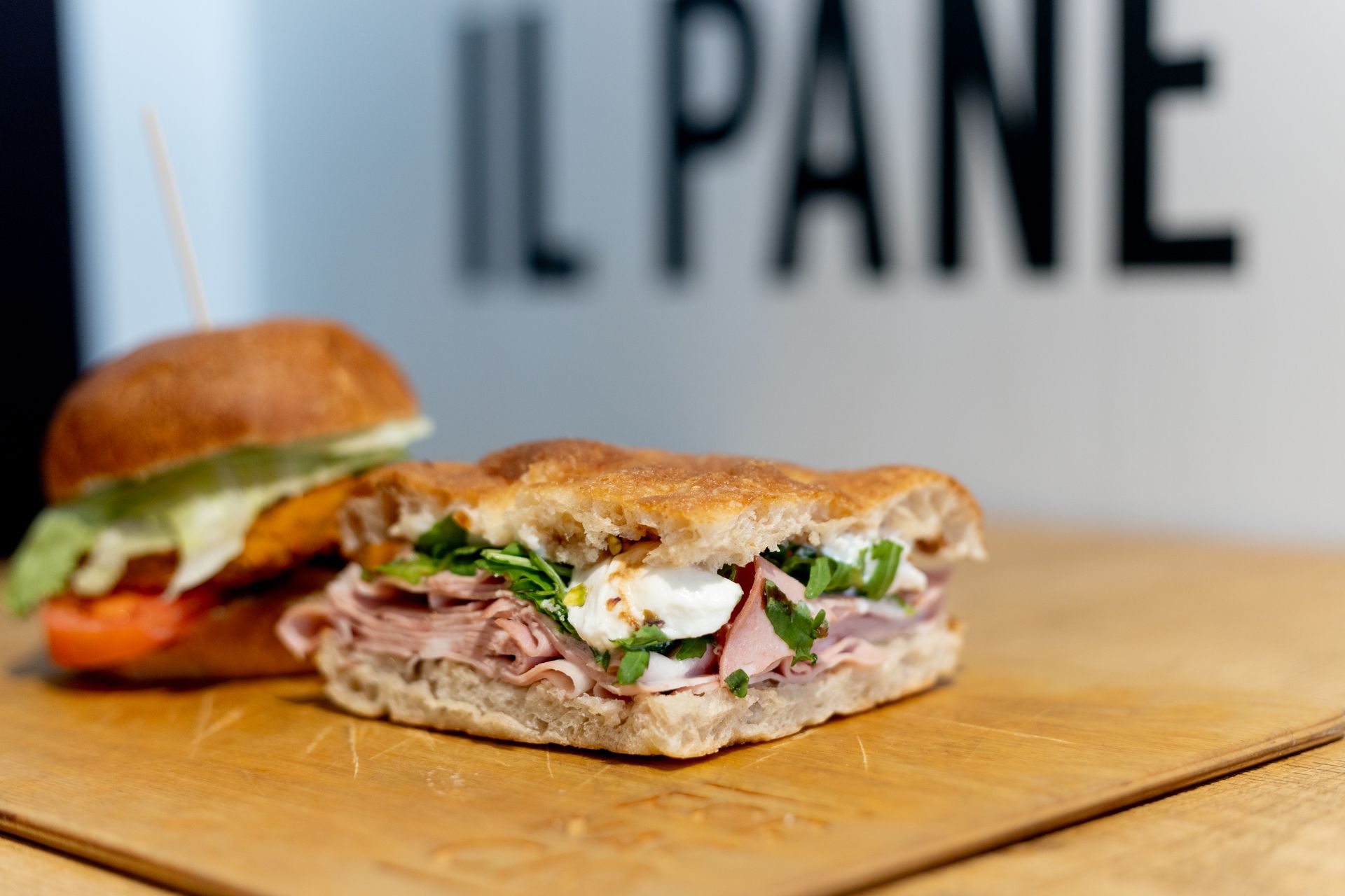 Due panini su un tagliere di legno; uno rotondo, uno quadrato, davanti al cartello “IL PANE”.