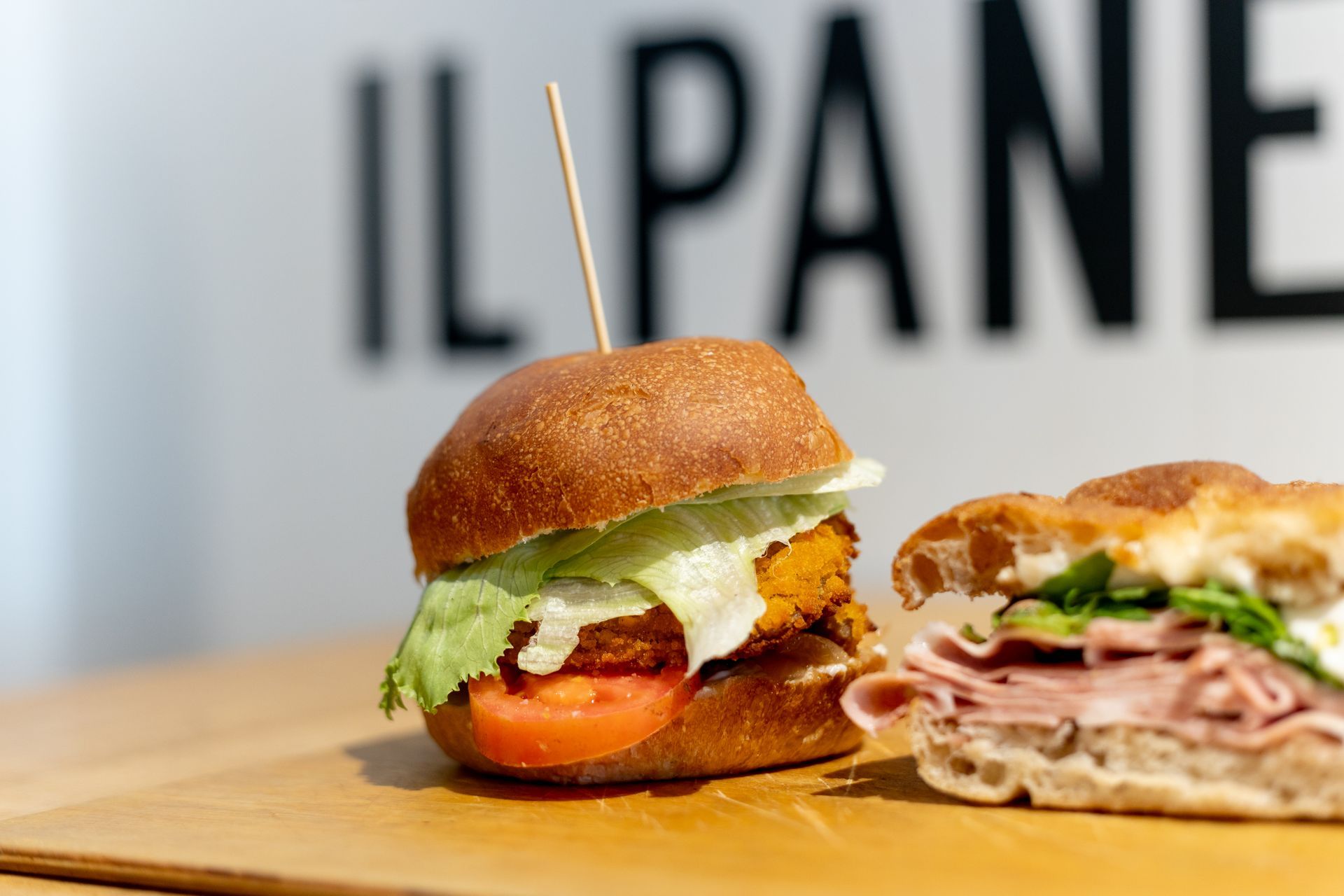 Due panini su un tagliere di legno; uno con cibo fritto, lattuga e pomodoro; l'altro con carne e verdure.