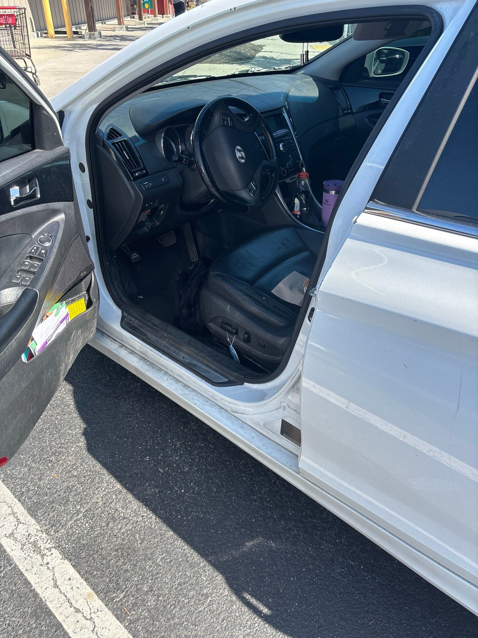 A white car with the door open is parked in a parking lot.