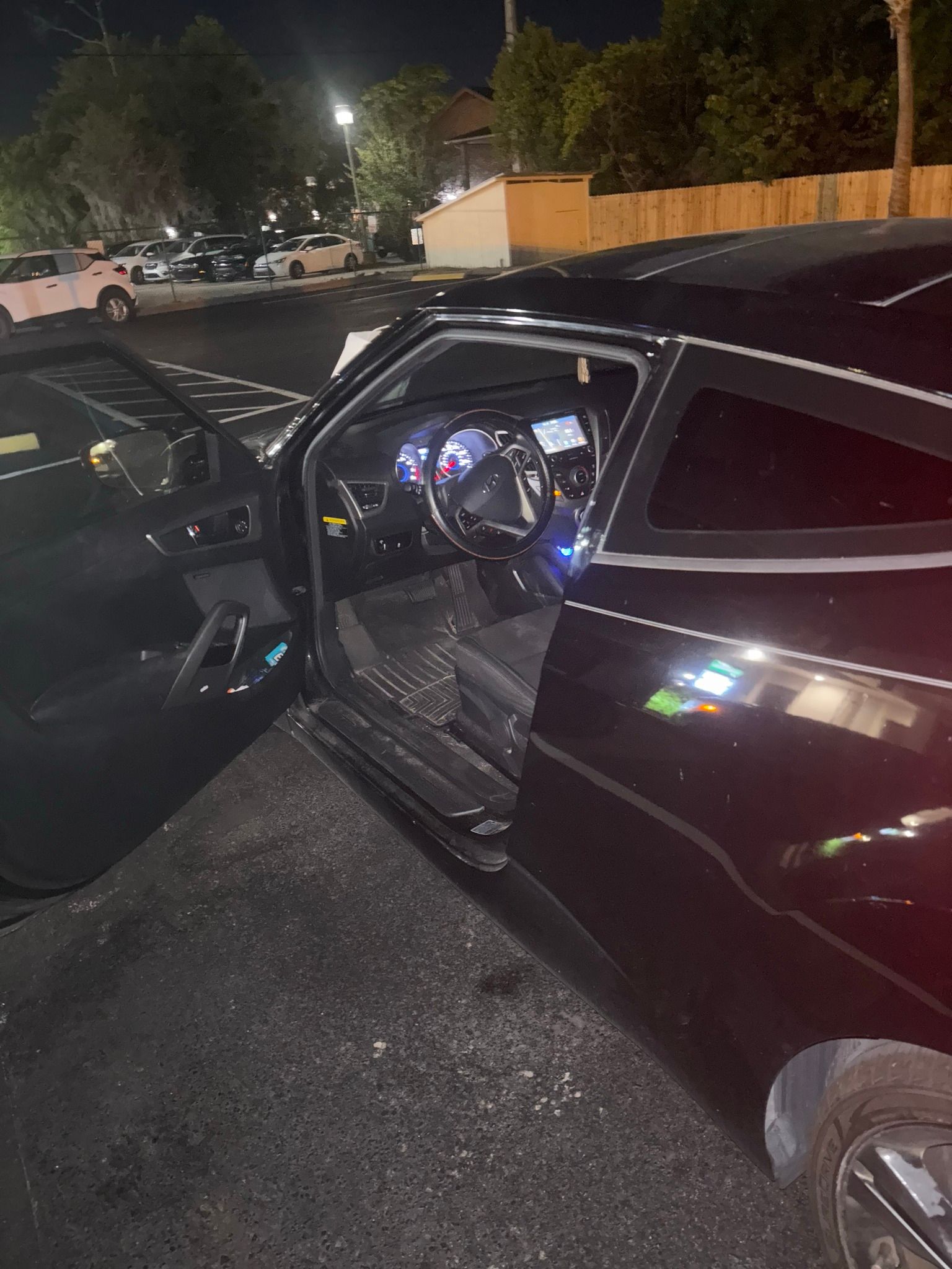 A black car with its doors open is parked in a parking lot at night.