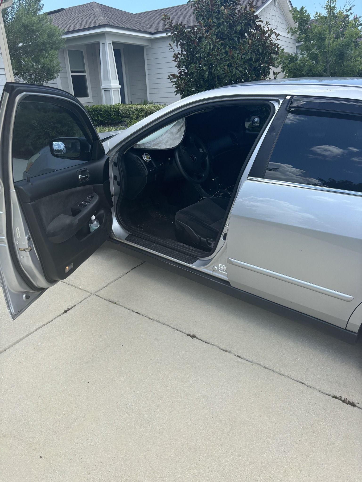 A silver car is parked in a driveway with its doors open.