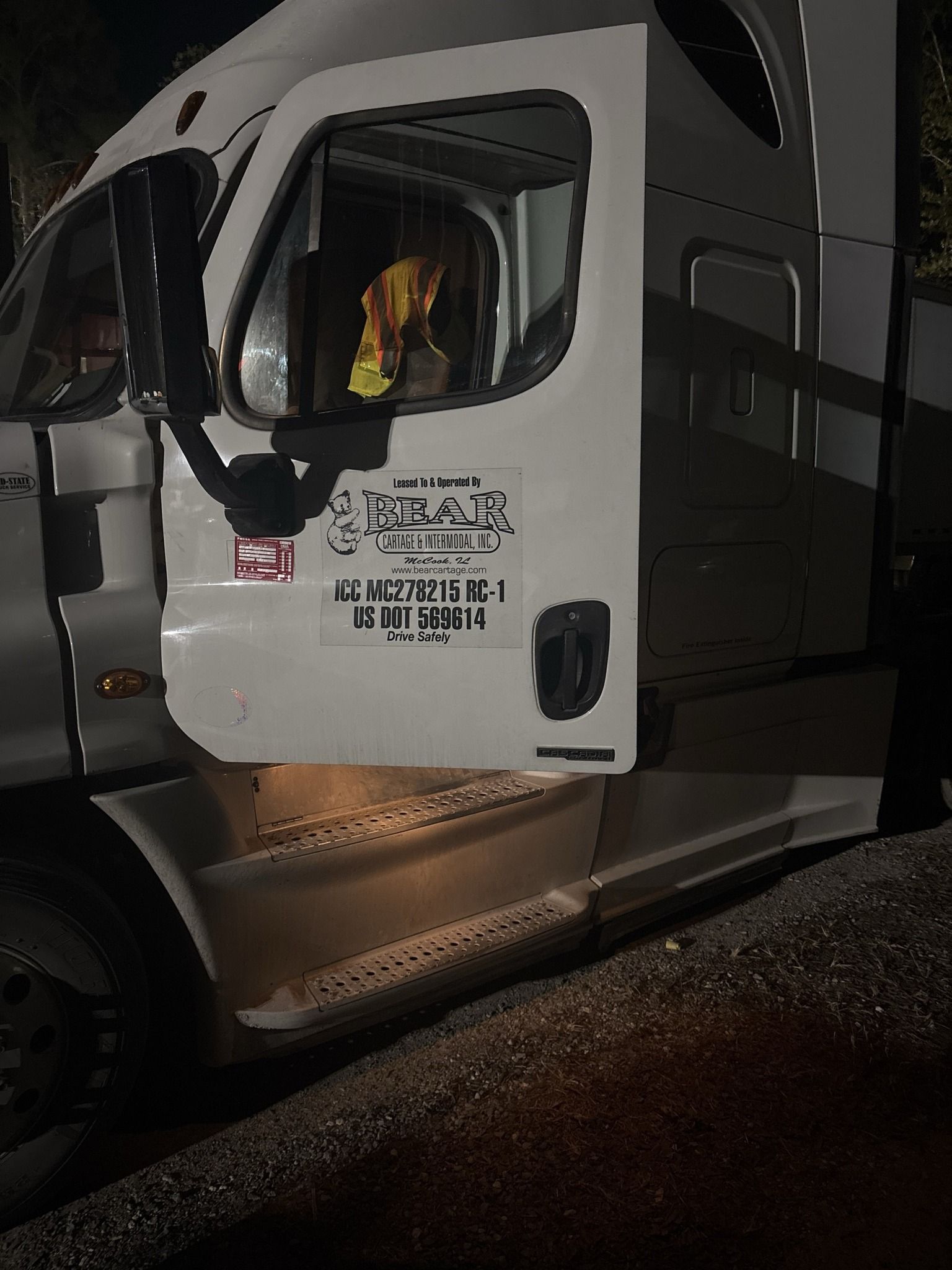 A white semi truck is parked on the side of the road at night.