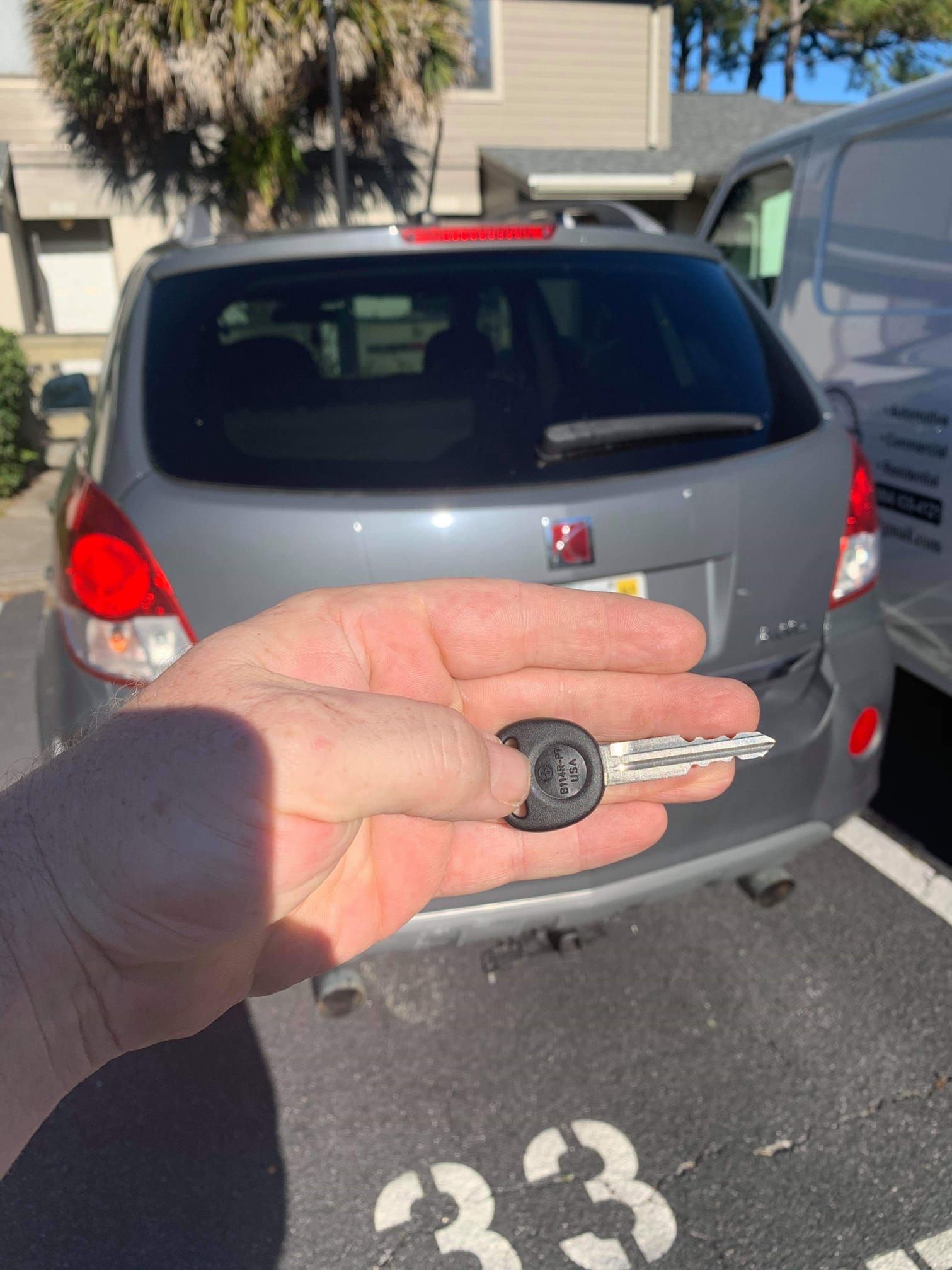 A person is holding a car key in front of a parked car.
