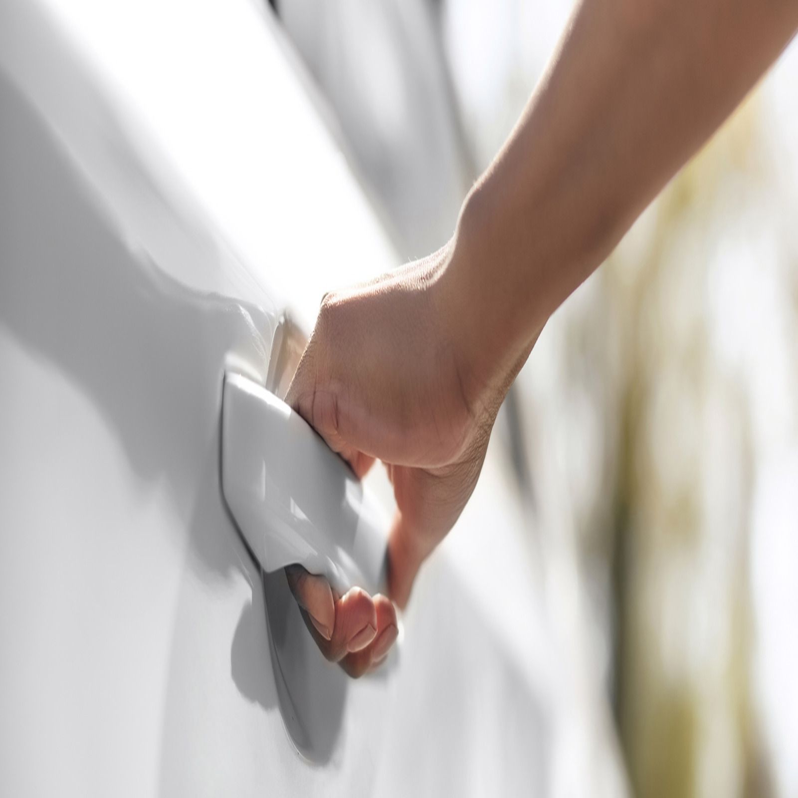 Hand opening a white car door handle.