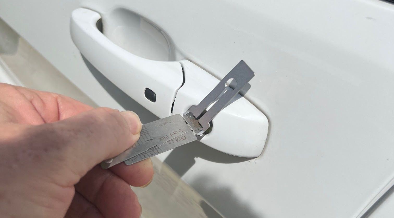 Hands holding and working on a car door lock cylinder; blue car in background.