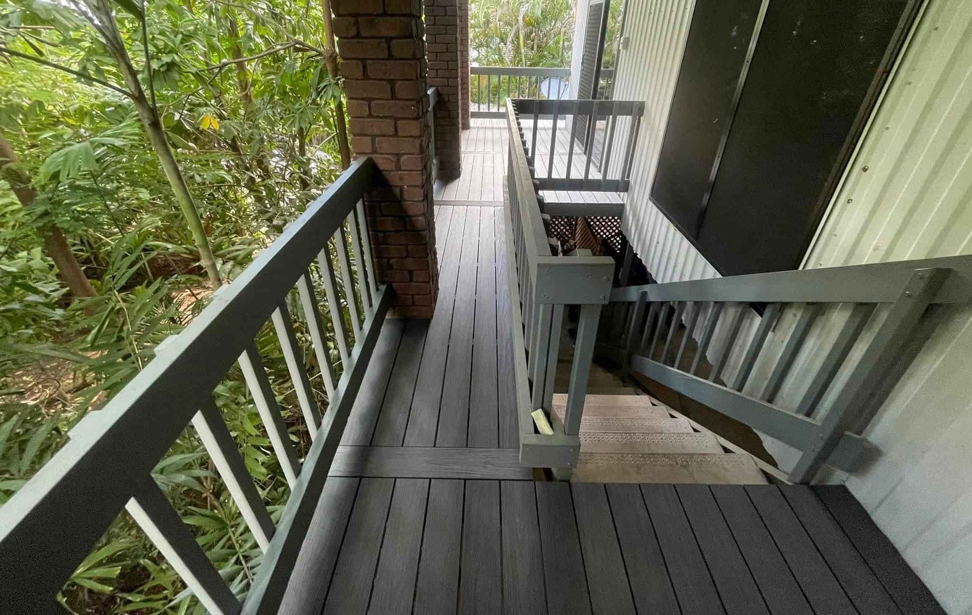A Gray Wooden Deck With Stairs Descends From a Building Into a Lush Green Forest — Northco Constructions In Muirhead, NT