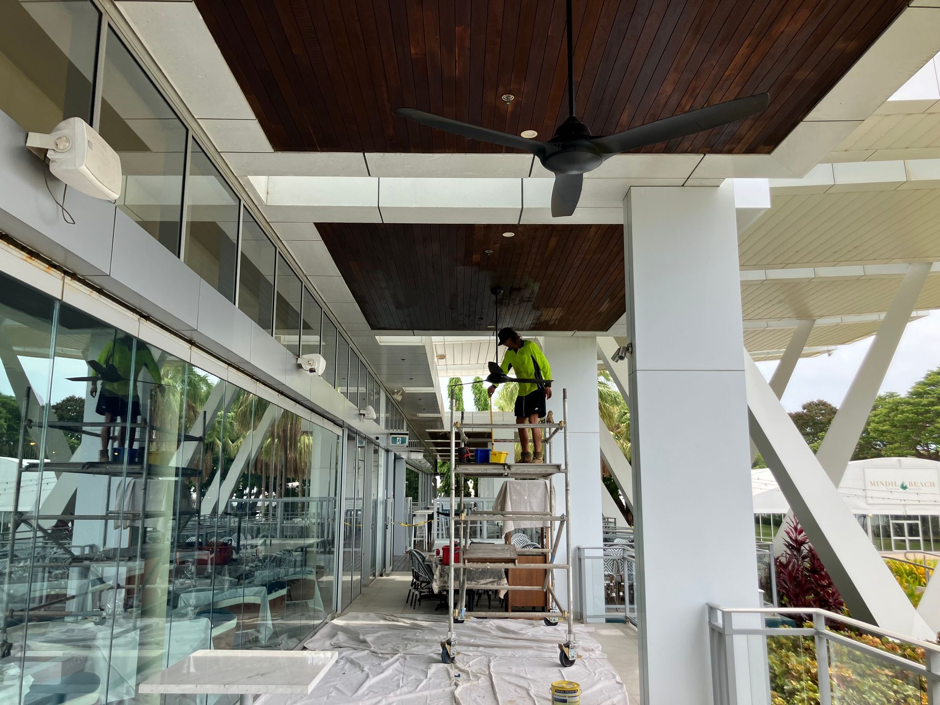 Person on Scaffolding Painting a Dark Brown Ceiling Outdoors — Northco Constructions In Muirhead, NT