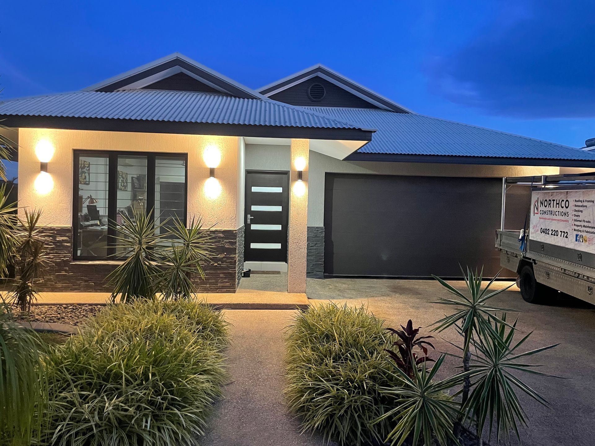 Modern House With Garage, Dark Door, And Exterior Lights At Dusk — Northco Constructions In Muirhead, NT