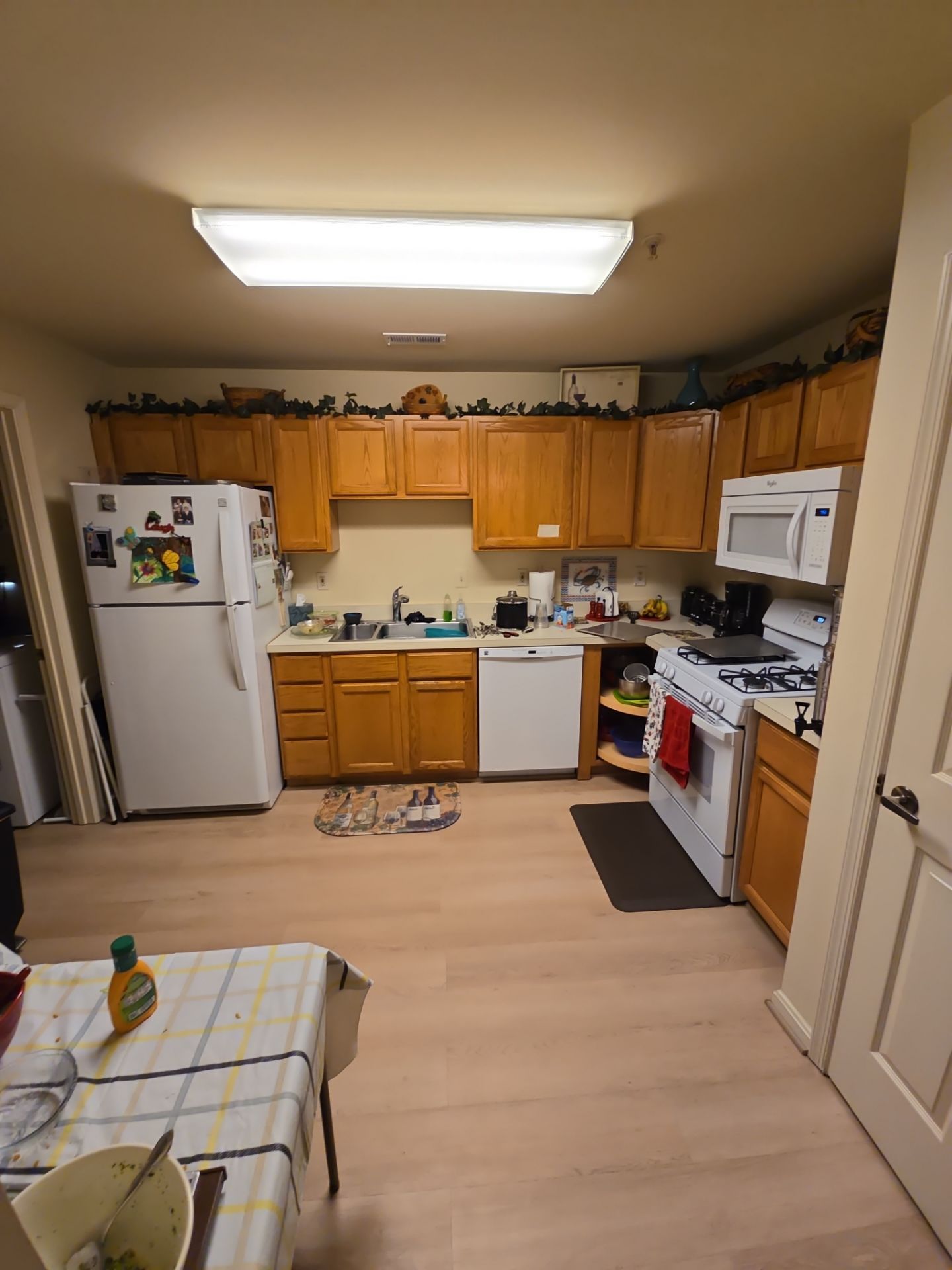 A kitchen with wooden cabinets , a refrigerator , a stove , a microwave , and a table.