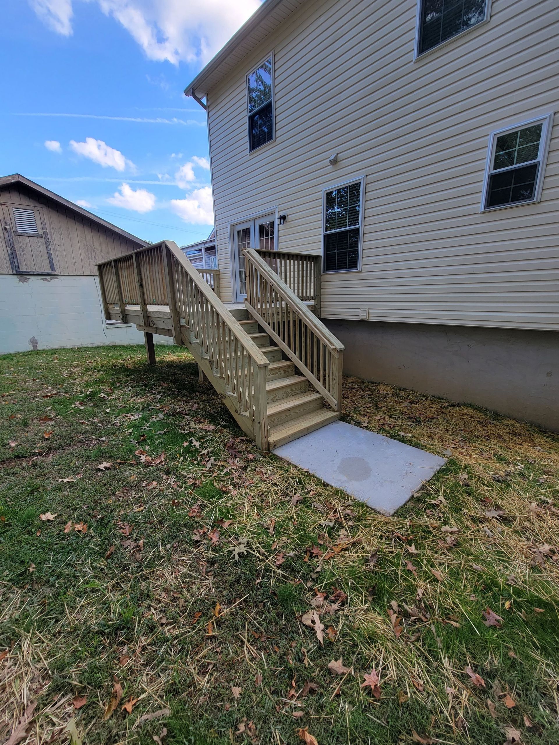 A wooden deck with stairs leading up to it is in the backyard of a house.