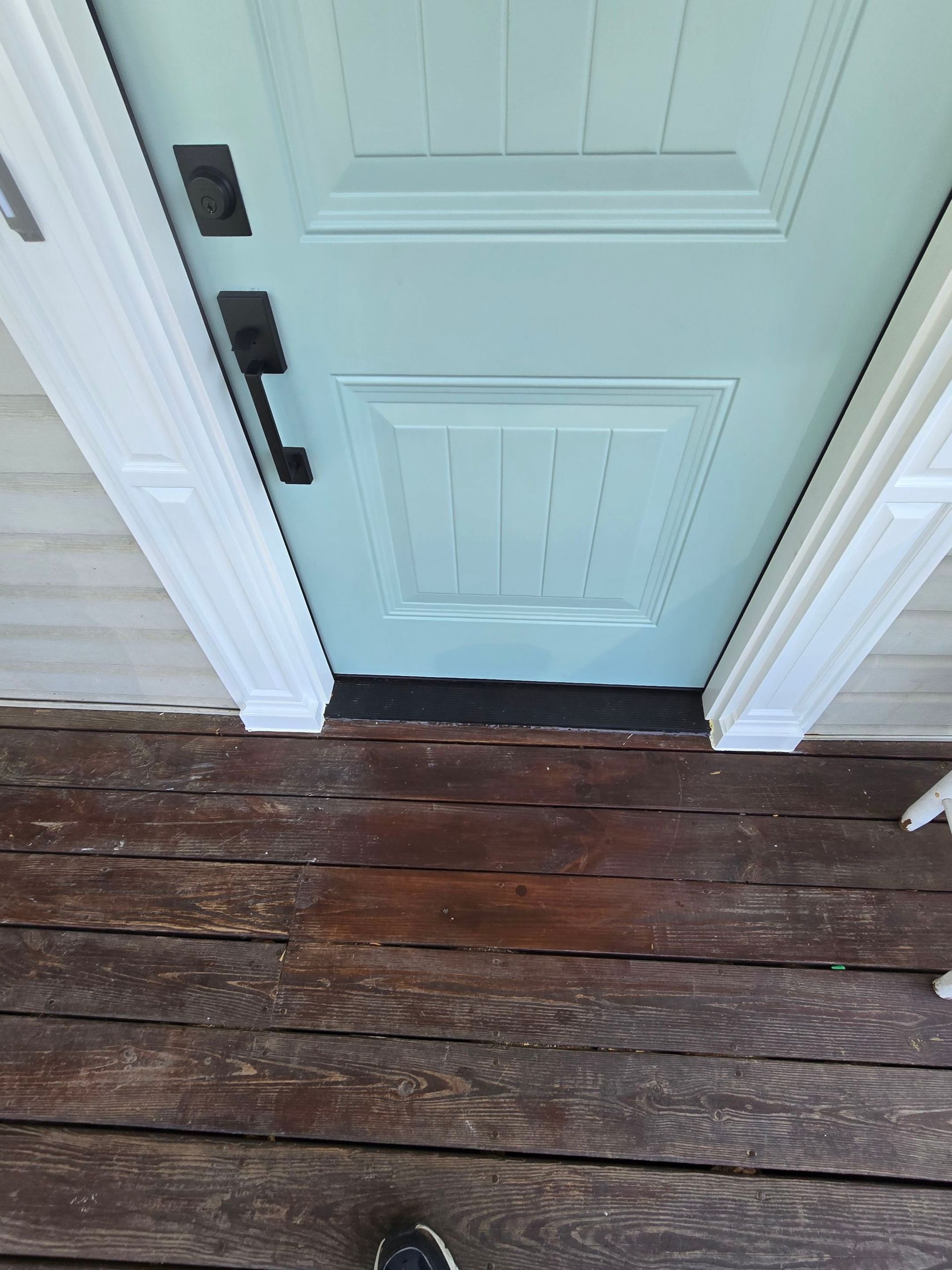 A person is standing in front of a blue door on a wooden deck.