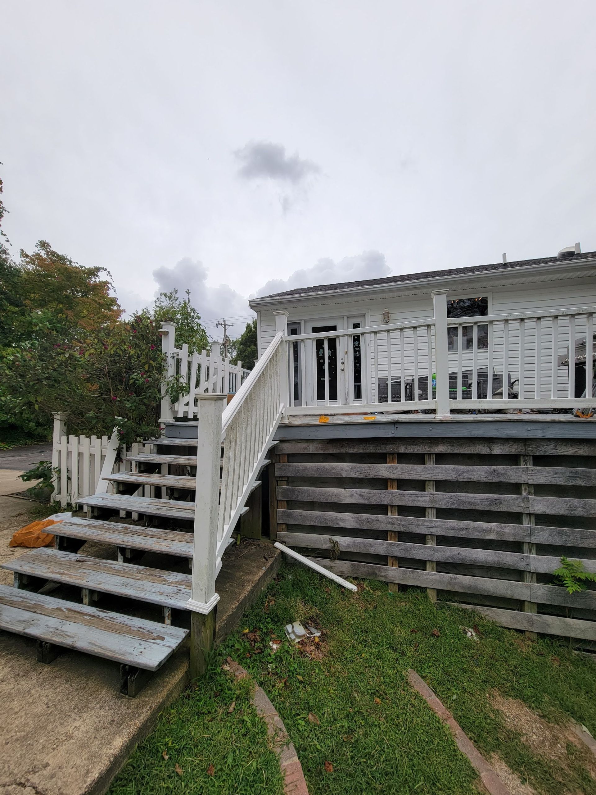 A white house with a deck and stairs leading up to it.