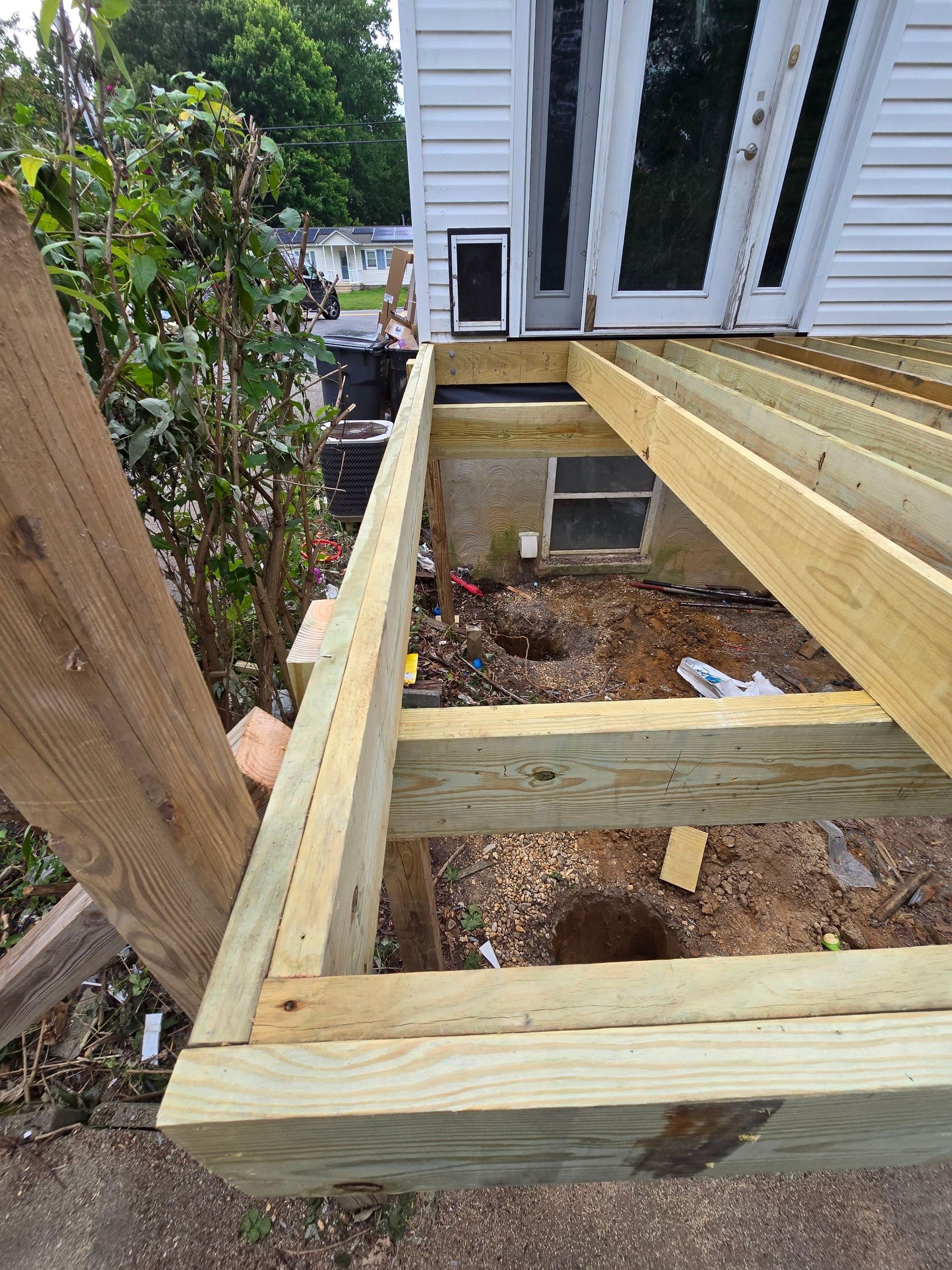 A wooden deck is being built in front of a white house.