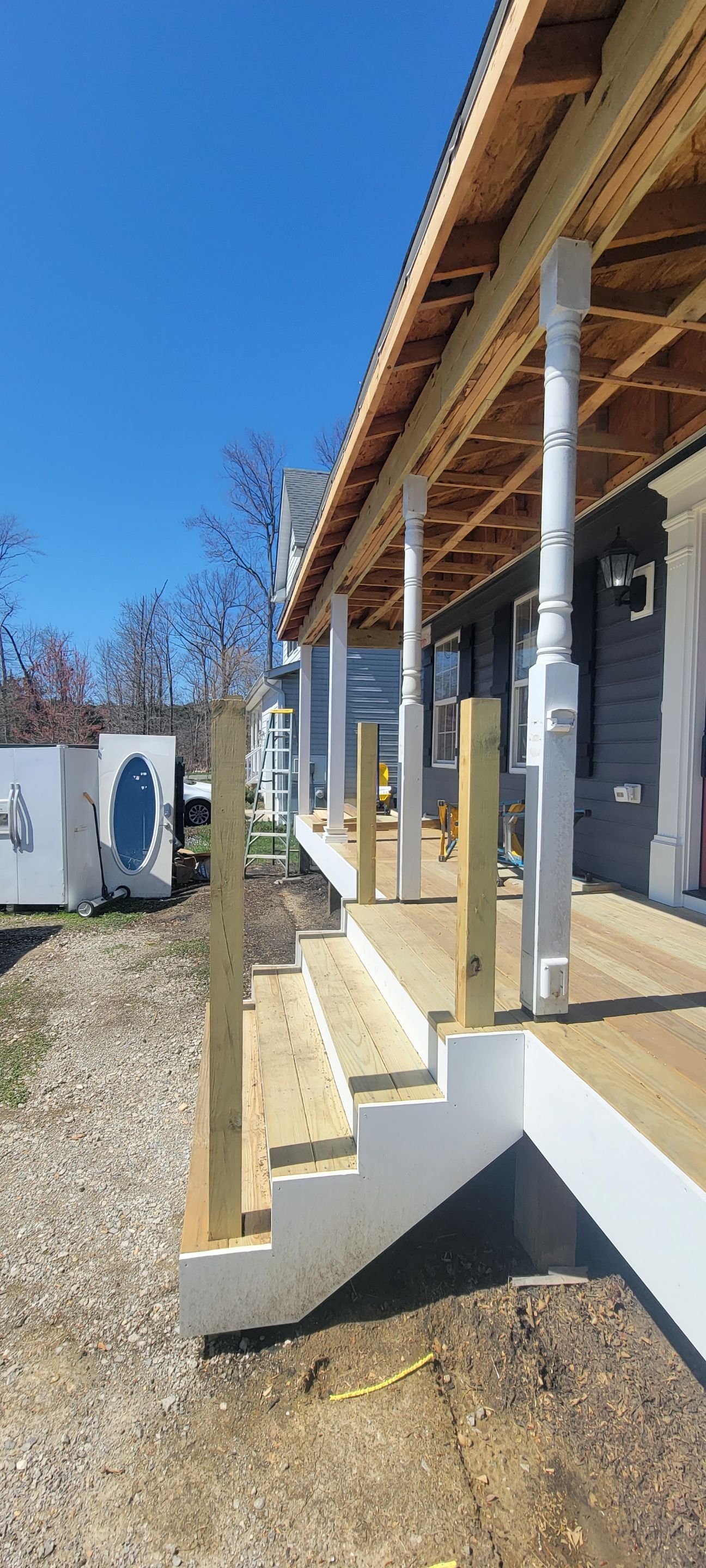 A porch with stairs and a wooden roof is under construction.